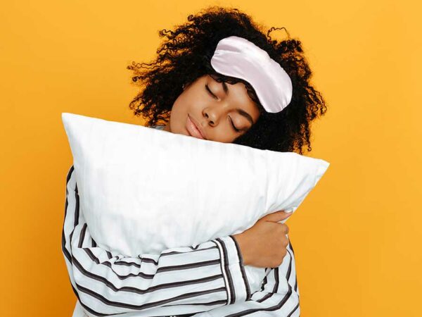 Sleeping. Dreams. Woman portrait. Afro American girl in pajama is hugging a pillow, on a yellow background